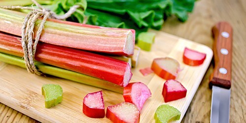 Bundle of stalks rhubarb, rhubarb pieces with a sheet, a knife on a wooden boards background