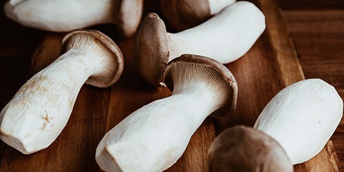 Group of raw King Oyster mushroom (also known as eryngii) on a wooden cutting kitchen board.