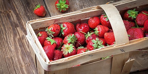 Fresh strawberries in a basket on a wooden table.